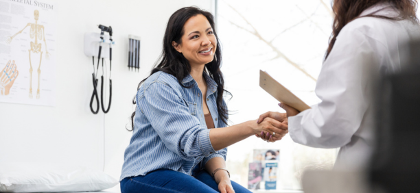 Young woman smiles and shakes hands with her doctor.