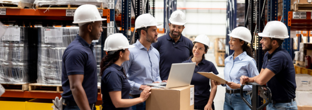 Group of employees wearing hard hats talking in a warehouse.