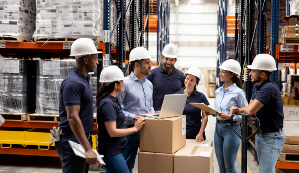 Group of employees wearing hard hats talking in a warehouse.